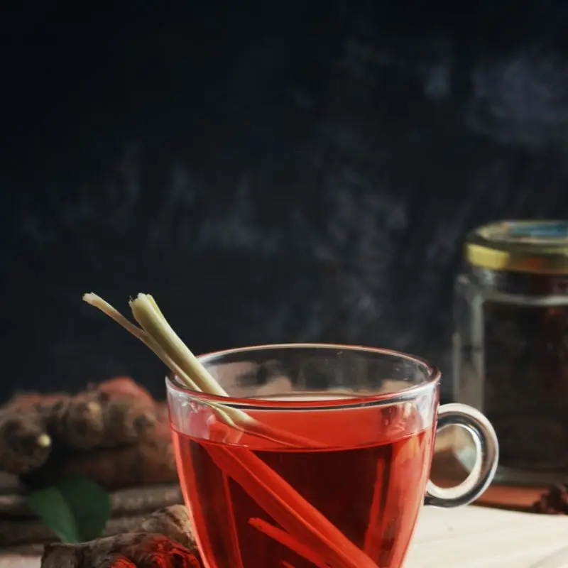 A cup of red herbal tea garnished with lemongrass stalks