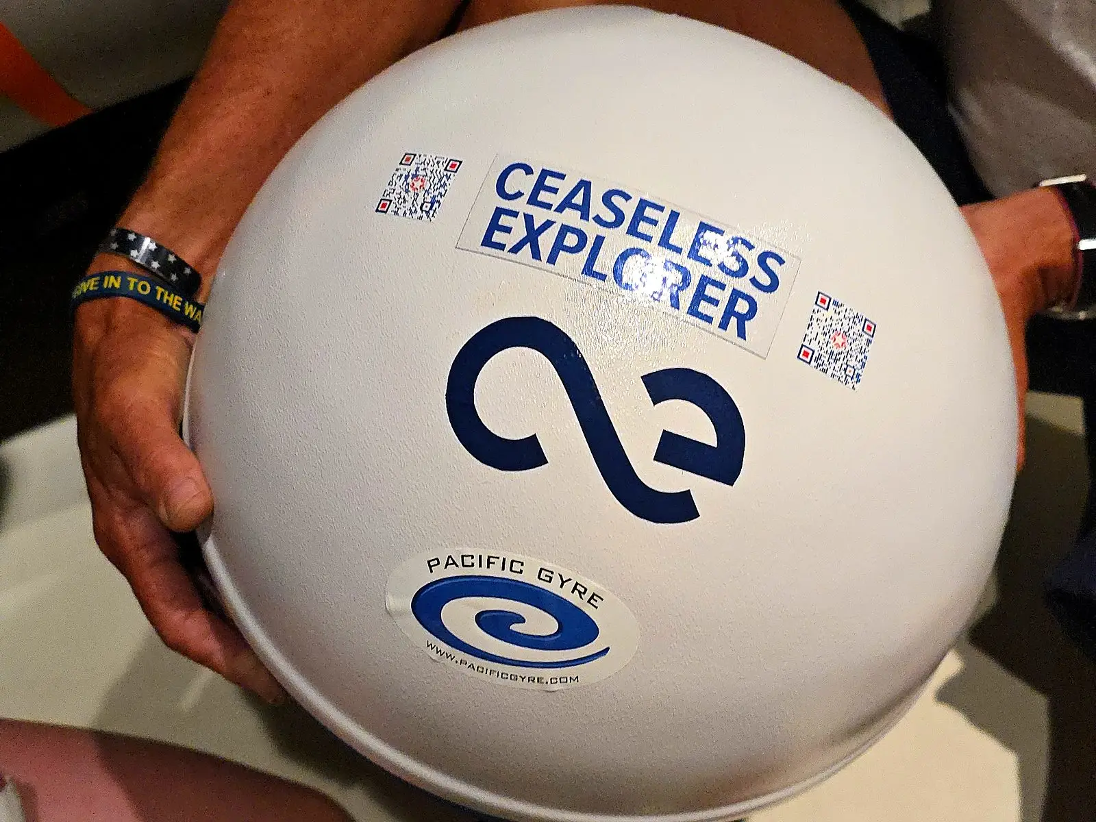 Una boya blanca Sea Drifter de la NOAA con una calcomanía de Ceaseless Explorer, sostenida por un tripulante antes de su despliegue