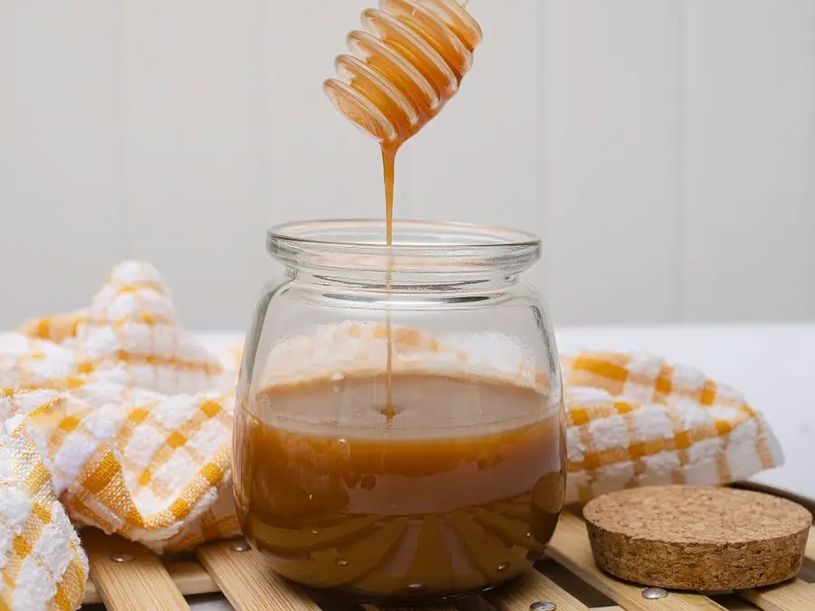 Honey being drizzled from a dipper into a glass jar