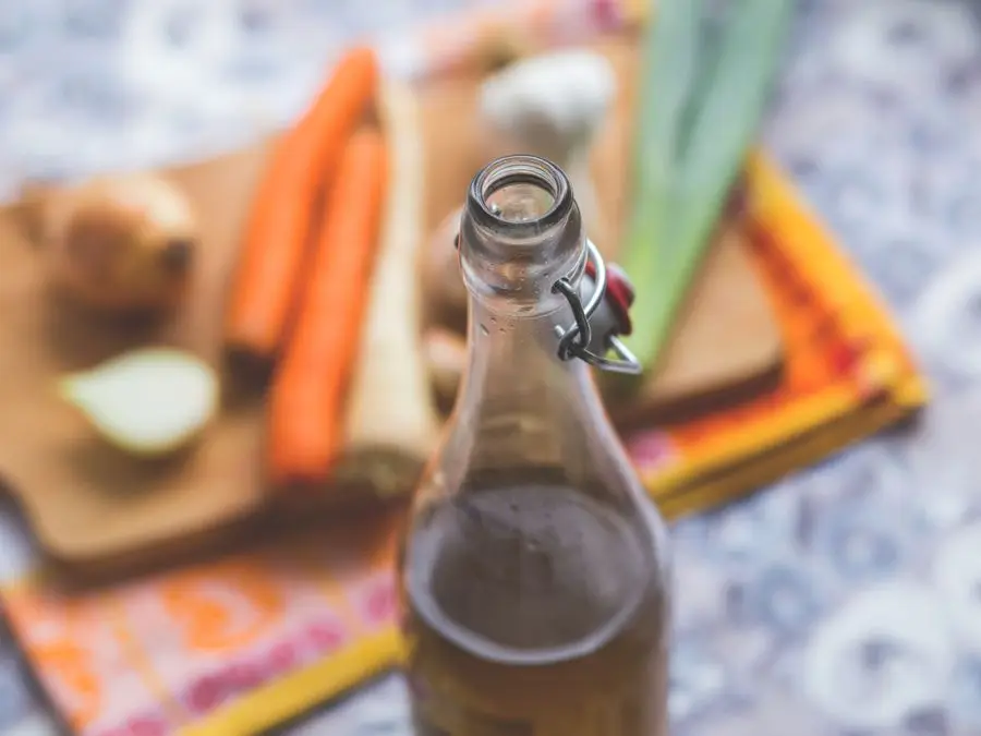 A glass bottle of vinegar with fresh vegetables in the background