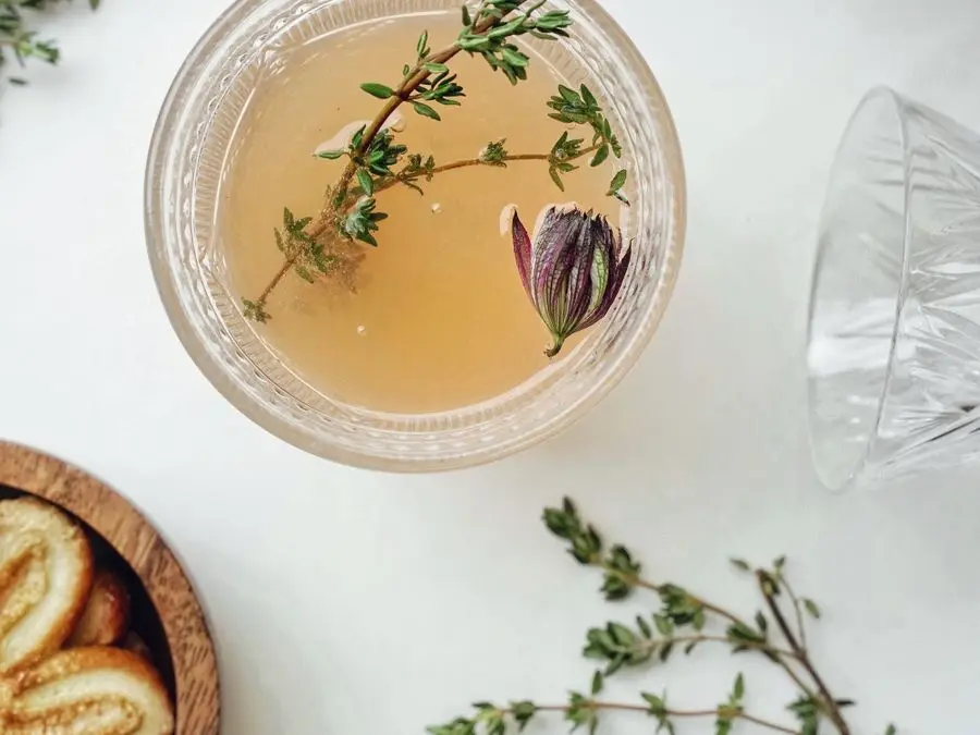 A glass of herbal iced tea garnished with fresh herb sprigs
