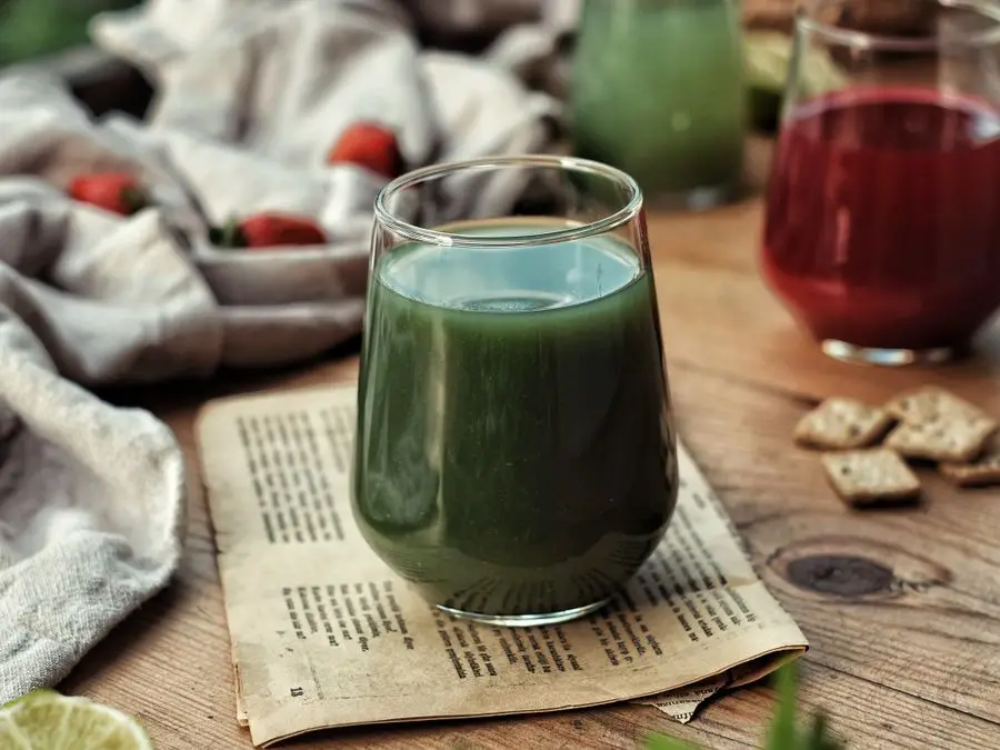 A glass of green vegetable juice on a wooden table beside fresh strawberries
